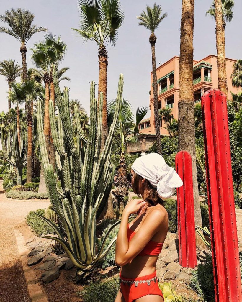 Woman in a red bikini wearing a white bandana surrounded by green cacti.