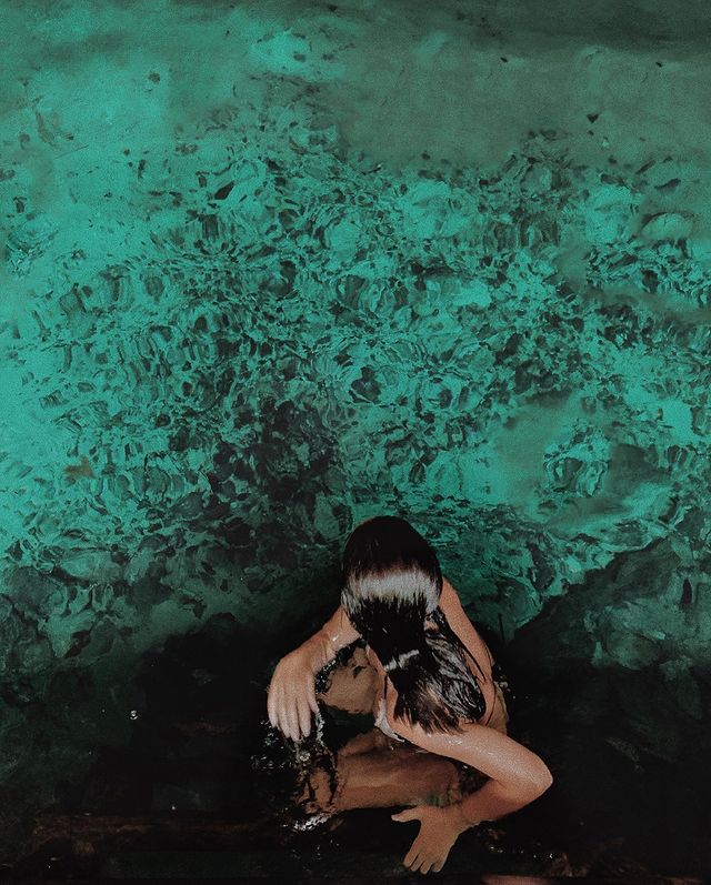 Woman swimming in teal water within a cave.