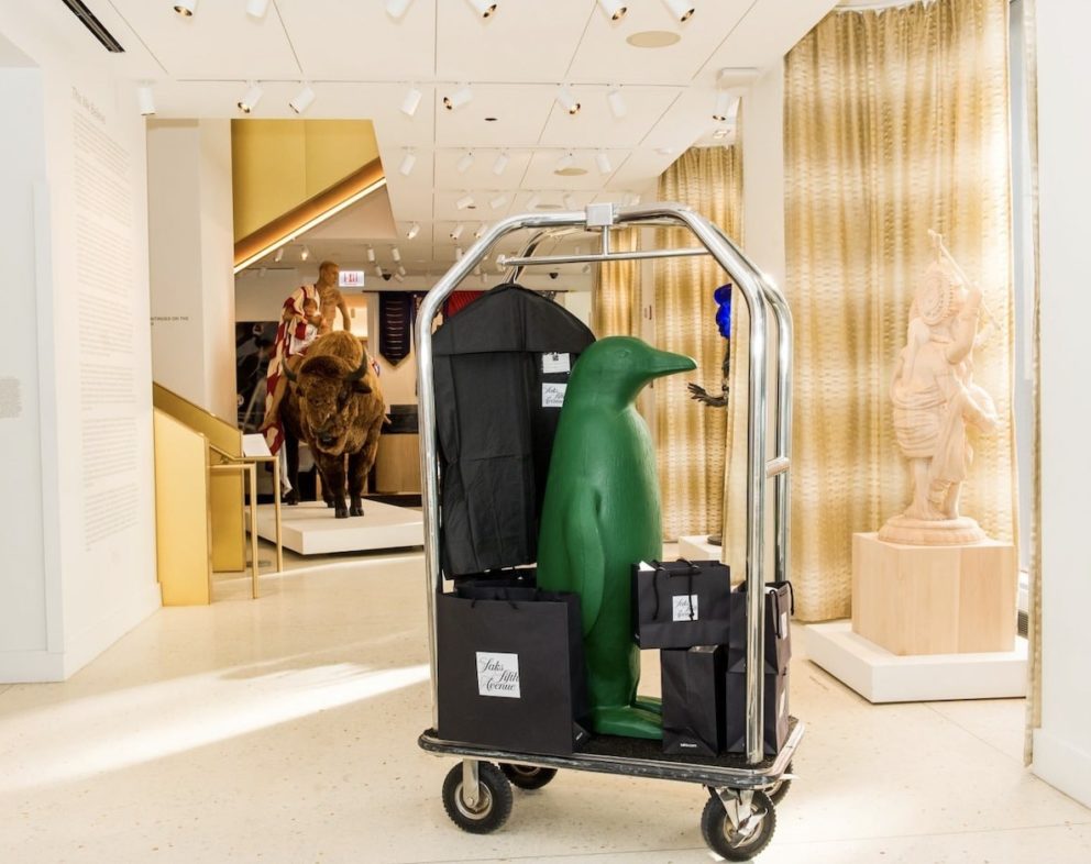 Luggage cart with a green penguin sculpture. Next to it are other animal sculptures.