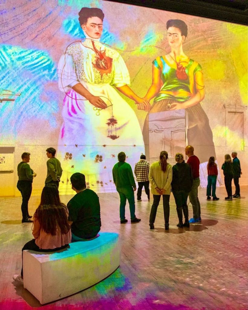 People looking at a large mural of Frida Kahlo at an immersive exhibition.
