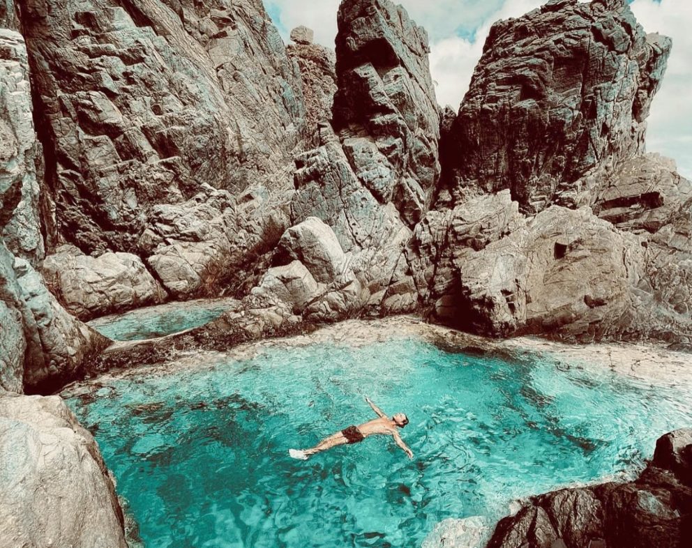 Man happily floating in turquoise pool surrounded by towering rock walls
