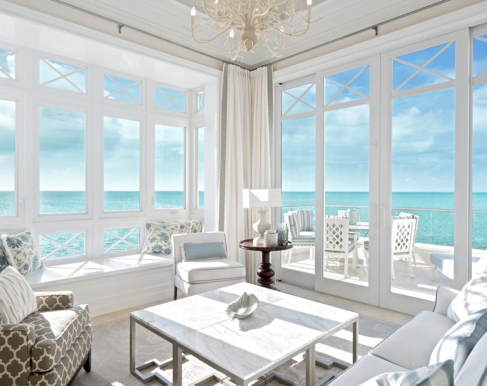 Room with white chairs and table and large windows overlooking the bright blue ocean.