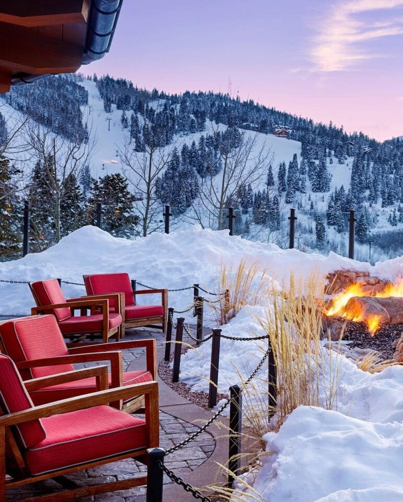 Red outdoor chairs next to a fireplace surrounded by snow and a ski slope.