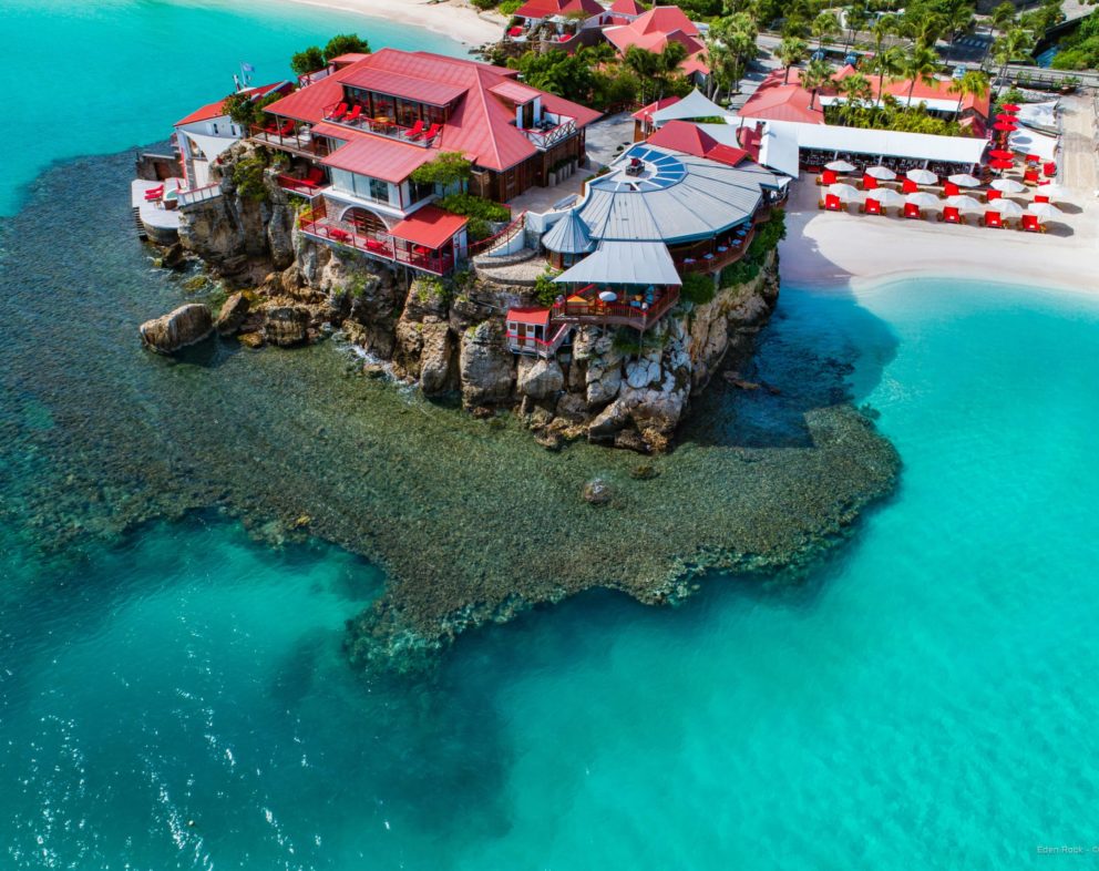 Hotel located next to bright blue water and a white sand beach.