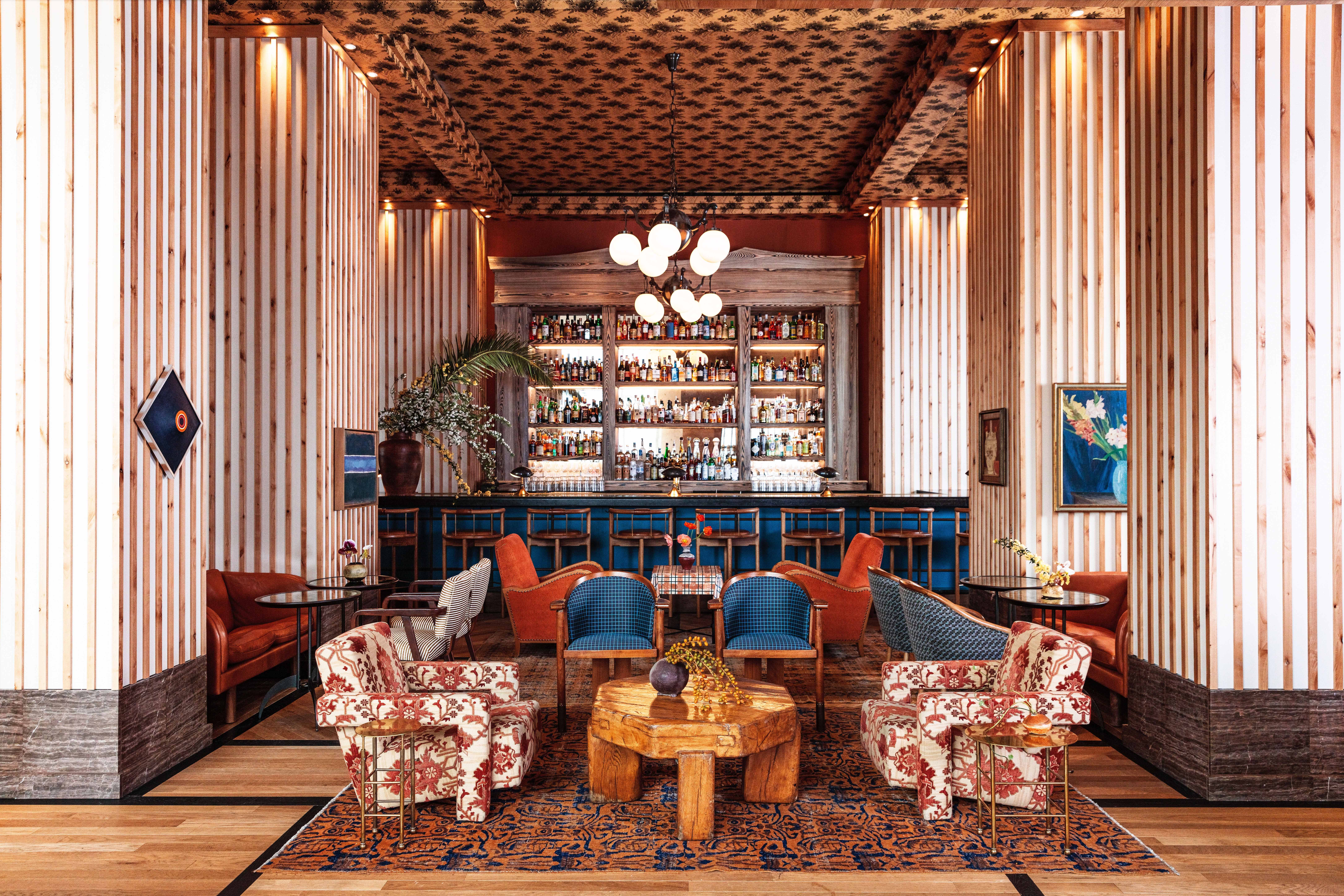 Lobby of a hotel with various patterned chairs and a bar in the back.