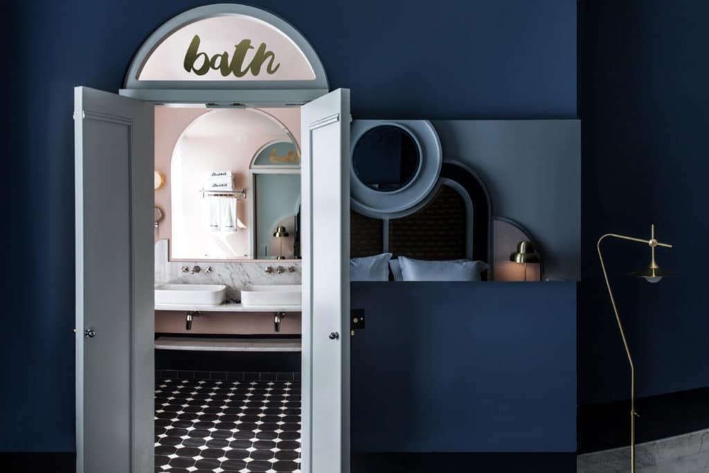 Blue room leading into a bathroom that has two sinks, a mirror, and black and white tiles.