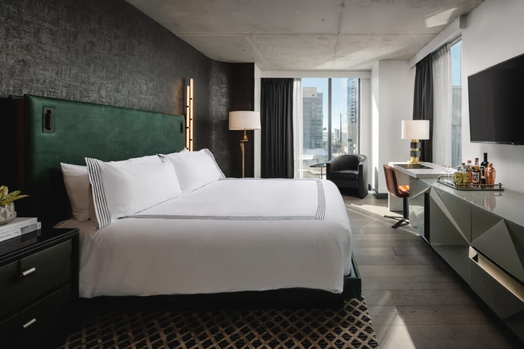 Hotel room with a bed with a green headboard, a dark green end table, and other upscale, modern furnishings.
