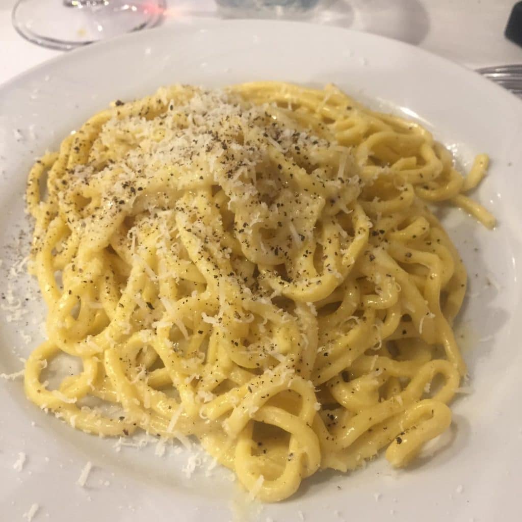 Pasta carbonara with cheese and pepper served on a white plate.