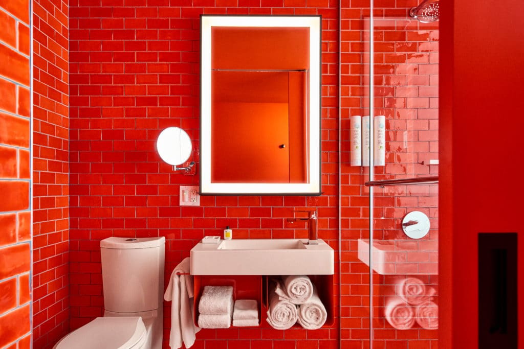 Bathroom with bright red bricks. There is also a sink and shower in the room.