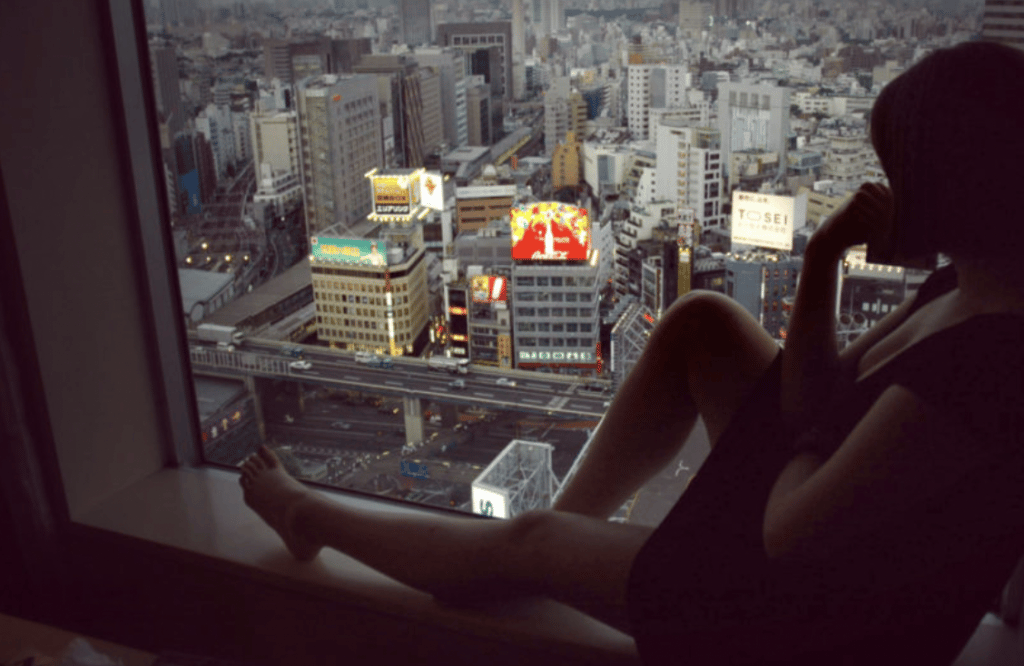Scene from the movie Lost in Translation where a woman is looking out her window which overlooks a city skyline.