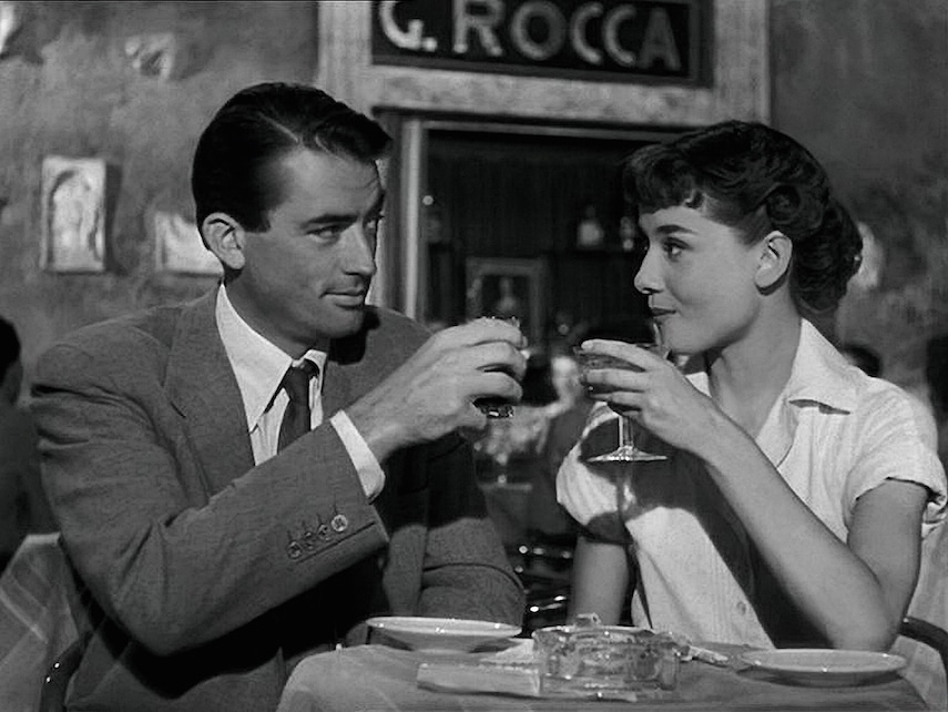 Scene from the movie Roman Holiday where a man and a woman are ready to clink their wine glasses with each other.