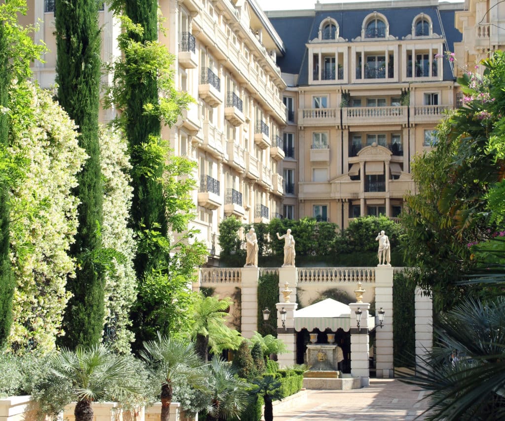 Hotel in Monte Carlo with ultra-elegant Belle Époque facade and green trees and bushes.