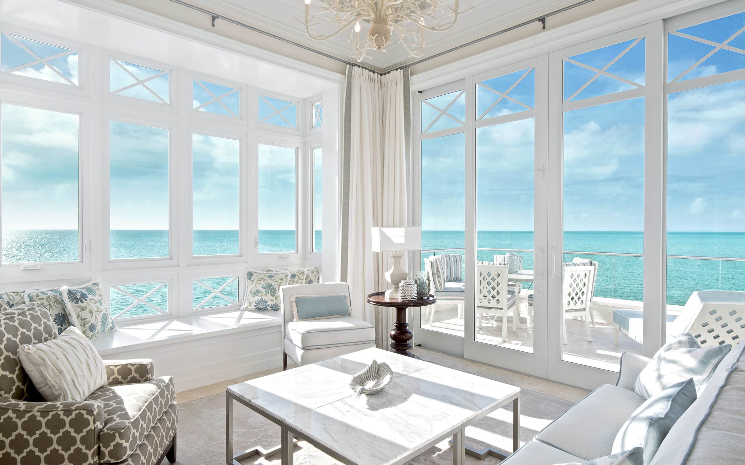 Room with white chairs and table and large windows overlooking the bright blue ocean.