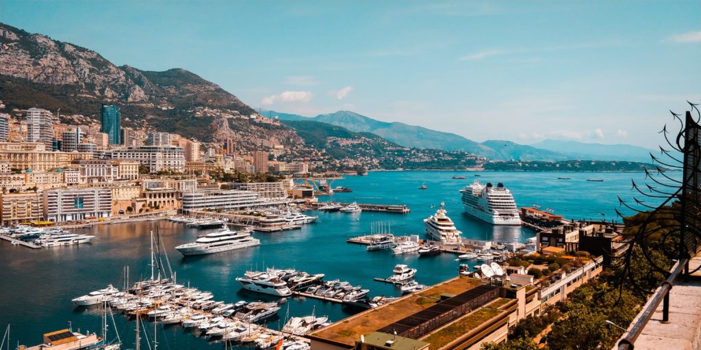 Panoramic view of Monaco. There are ships in the bay and mountains in the background.
