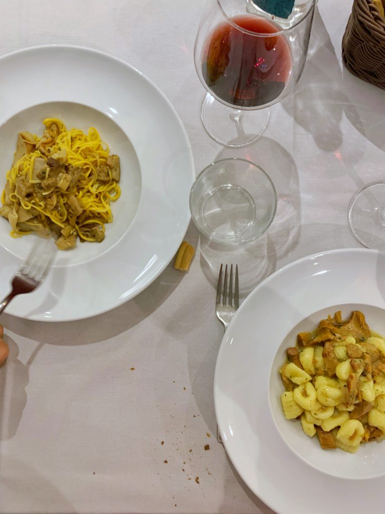 White plates with different types of pasta and a glass of wine on a white table in Italy.